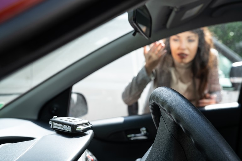 a woman is locked out of her car and visibly frustrated seeing that she left her car keys on the dashboard