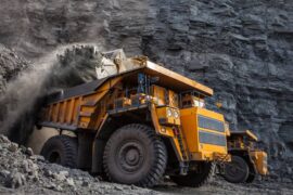 a big yellow mining truck loads some coal in a big coal mine. Another big mining truck behind this truck is doing the same.