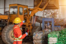 A foreman in a factory wearing a uniform and safety gear while overseeing waste management operations.