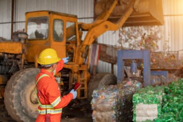 A foreman in a factory wearing a uniform and safety gear while overseeing waste management operations.