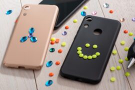Two phone cases, one black and one pink, being decorated with plastic studs and crystals. A hot glue gun rests to the side.