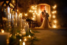 A couple dances at their outdoor wedding venue at night, surrounded by warm string lights with no guests around.