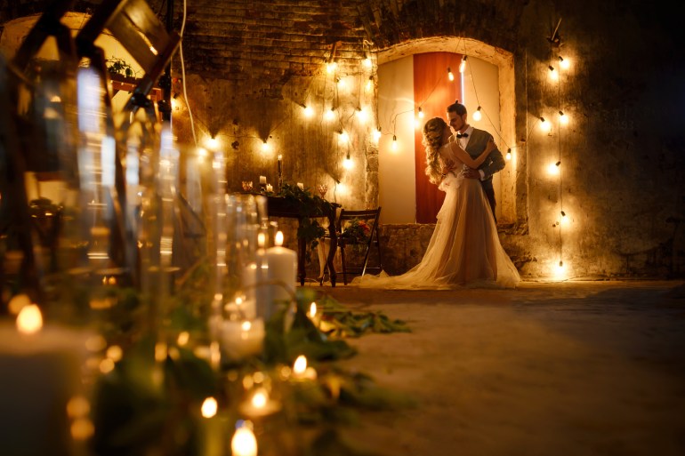A couple dances at their outdoor wedding venue at night, surrounded by warm string lights with no guests around.