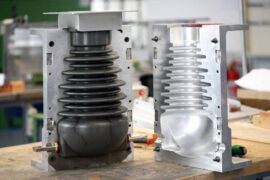 Metal mold open showing a finished plastic gray pump. It's sitting on a wooden table inside of an industrial environment.