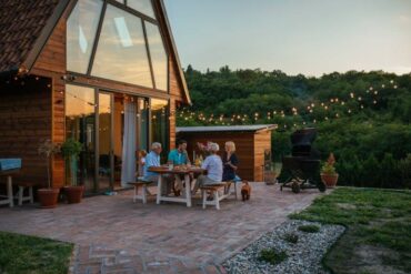 A family sits in a home backyard on a bench at sunset with string lights and lots of greenery behind them.