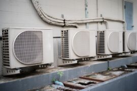 A series of air conditioner condensers sitting outdoors on a wall that may require some maintenance.