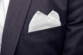 A close-up of a pocket square inside of a breast pocket. The pocket square is white with tiny patterns on it.