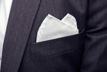 A close-up of a pocket square inside of a breast pocket. The pocket square is white with tiny patterns on it.