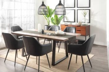 A dining room with black chairs around a wooden table. There are plants and a wooden drawer in the room.