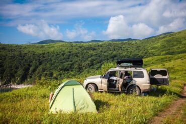 An overland vehicle parked on land next to a tent. The tent and vehicle are sitting on a mountain in some grass.