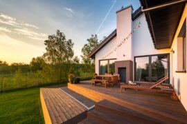 A modern home's wooden patio with lounging furniture. The patio has a view of a an orchard at sunset.