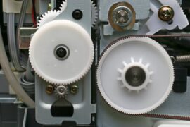 A machine with plastic cogs and metal cogs. The plastic cogs are white, and the metal cogs are gray.