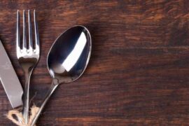 A wooden restaurant table with three pieces of silver cutlery wrapped in twine, including a knife, fork, and spoon.