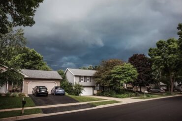 A suburban neighborhood with a few houses standing next to each other underneath a sky full of thunderstorm clouds.