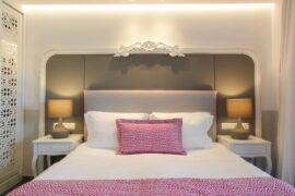 A bed with an upholstered headboard and white bedding with pink and white accents. The bed is flanked by two tables and lamps.