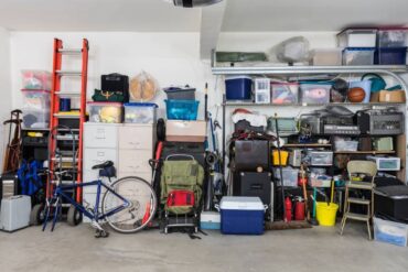 A room packed with clutter such as a bike, cooler, plastic bins and more all stacked against a white wall.