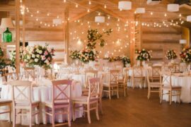 An indoor wedding reception area. The tables are covered in white tablecloths and there are fairy lights in the background.