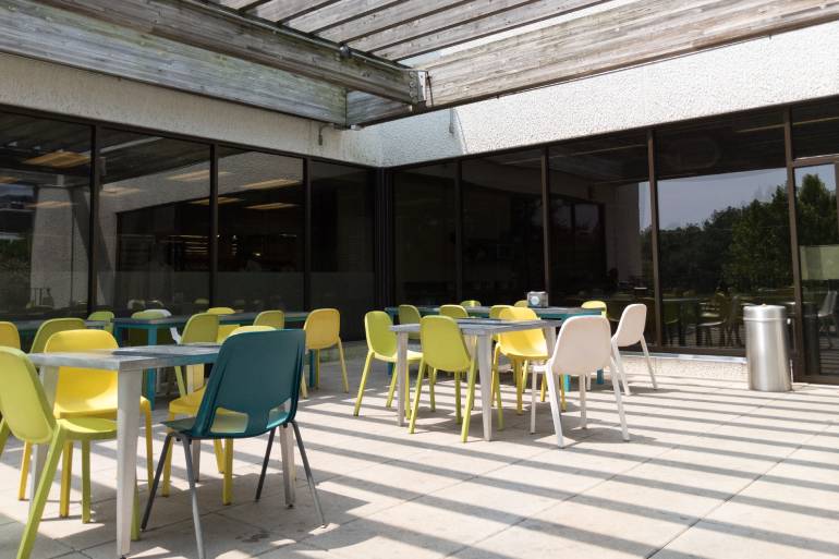An outdoor seating area at a business. There are tables and colorful chairs set up and wooden shade covering overhead.