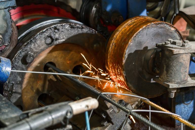 A machine in an industrial setting using a high-speed spinning wheel to create sparks and grind down metal wires.