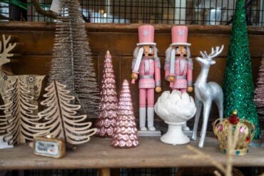 A shelf with a collection of holiday decor, including pink nutcrackers, wooden and tinsel trees, and a silver reindeer.