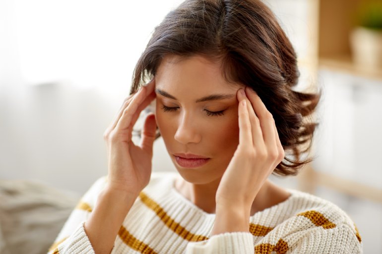 A woman has her hands to her temples with her eyes closed. Her hair goes back and she wears a striped sweater.