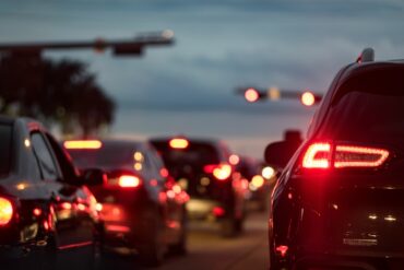 Several vehicles are stopped at a red light. Their breaklights and headlights illuminate the darkness.