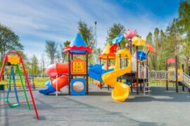 A colorful outdoor playground on a sunny day with several slides, swings, tunnels, and climbing towers.