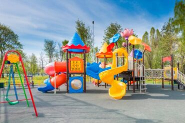 A colorful outdoor playground on a sunny day with several slides, swings, tunnels, and climbing towers.