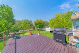 A backyard featuring a spacious deck, bordered by a combination of wood handrails and sleek cable railings.