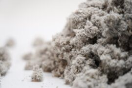 A pile of gray cellulose insulation with hints of black, white, and red set against a white background.