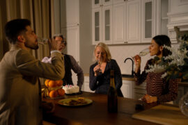 A group of friends gathered around the kitchen island in semi-formal attire taking a drink out of champagne flutes.