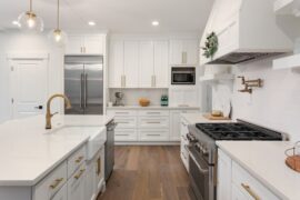 A modern kitchen with white cabinets, a large stove, pendant lights, and gold fixtures throughout.