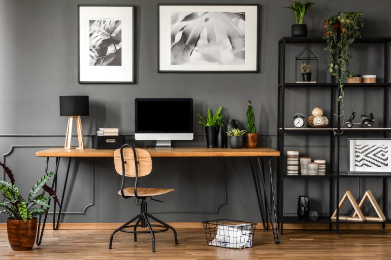 A neat and tidy home office featuring a wood and metal desk and chair next to a metal bookcase against a gray wall.