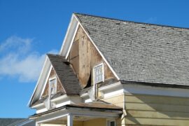 An older multi-story home that's falling apart on the outside. The siding is stripped away to wood paneling.