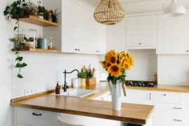 A bright kitchen with white cabinets and butcher block countertops. There's a white vase with sunflowers on the counter.