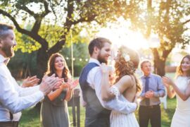 A smiling bride and groom dancing at an outdoor wedding reception as guests stand nearby and cheer them on.