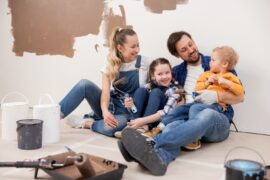 Two parents with their kids in their home with cans of paint and a roller in front of them during a wall painting project.