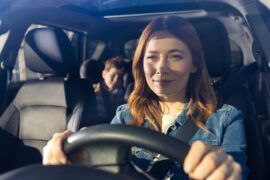 A smiling woman with a child looking ahead with determination while sitting in the driver seat of a vehicle.