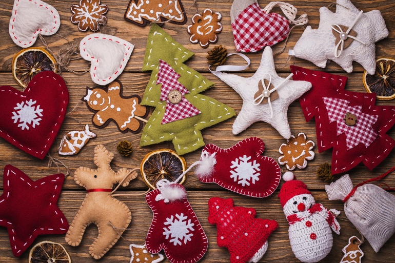A wooden table covered with a collection of handmade felt Christmas ornaments. They're red, green, and cream.