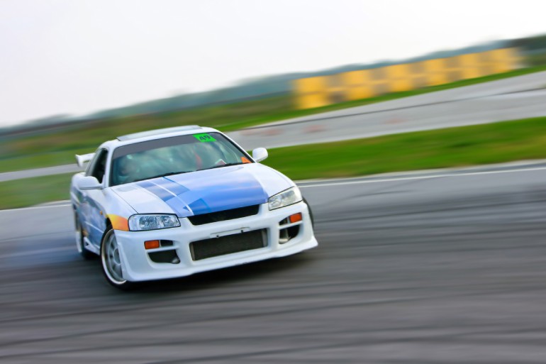 A frontal view of a white and blue sports car with a spoiler drifting around the corner on a race track.