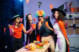A group of four young adults wearing Halloween costumes smile and dance at a party with Halloween décor.