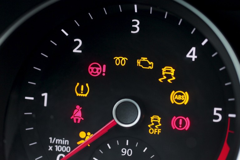 A close-up of a car's dashboard with various warning lights, including a check-engine light, seatbelt light, and more.