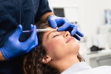A close-up of a beautician expert's hands injecting Botox into a young woman's forehead.