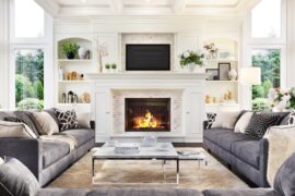 A large white fireplace with decorative shelves on either side. Three gray sofas form a U-shape in front of the fireplace.
