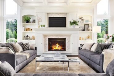 A large white fireplace with decorative shelves on either side. Three gray sofas form a U-shape in front of the fireplace.