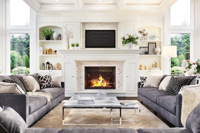 A large white fireplace with decorative shelves on either side. Three gray sofas form a U-shape in front of the fireplace.