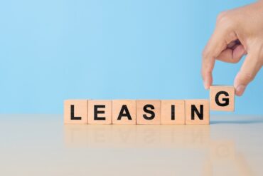 A hand adds a “G” block to a line of blocks spelling out the word “LEASING” on a blue background.