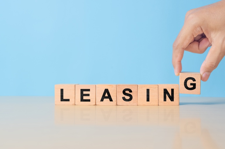 A hand adds a “G” block to a line of blocks spelling out the word “LEASING” on a blue background.