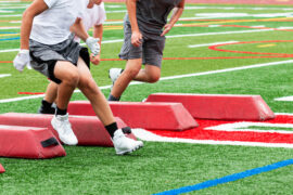 A trio of high school football players running between barriers on a painted football field to train.