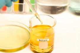 A glass beaker is filled with a yellow liquid and is labeled "solvent." A Petri dish is next to it, and a dropper is above it.